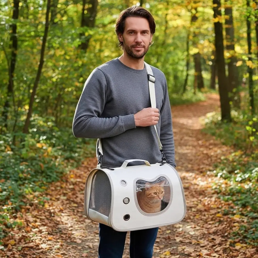 Chat roux dans un sac de transport blanc avec bandoulière, porté par un homme en promenade dans une forêt.